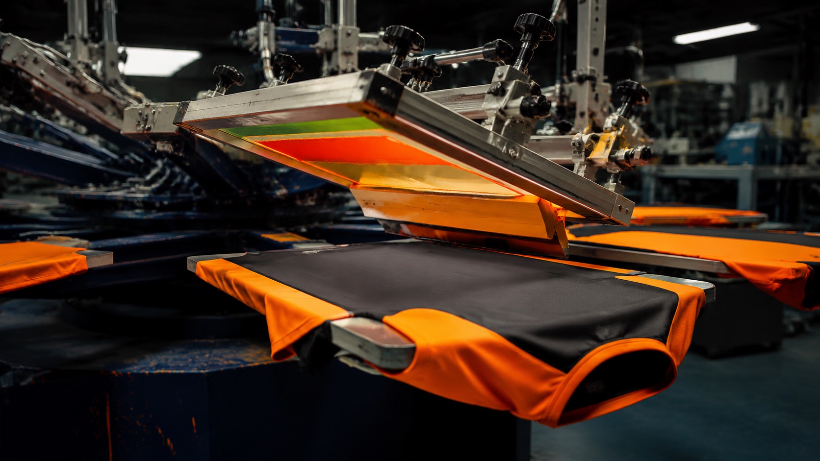 Rotary screen printing carousel pressing ink through a mesh screen onto garments in a workshop