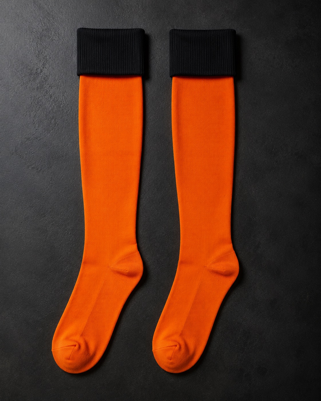 Orange football socks with black ribbed turnover, flat lay on dark charcoal