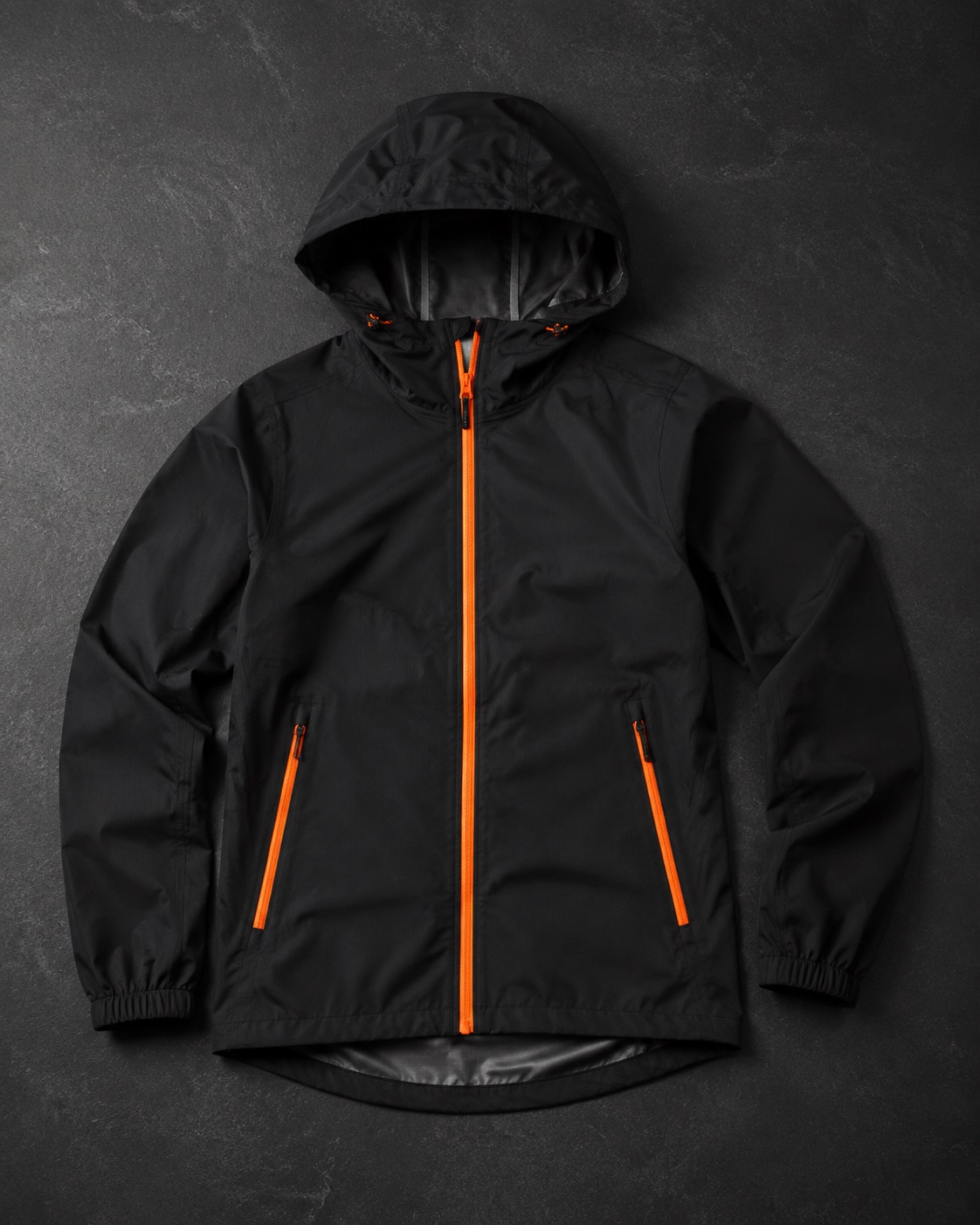 Cricket rain shell jacket with zip, flat lay on dark charcoal