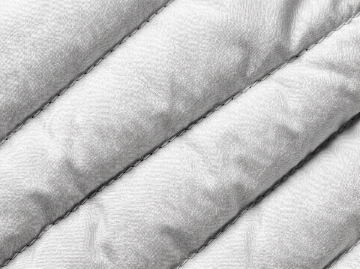 Extreme macro of white quilted padded fabric showing stitched channels