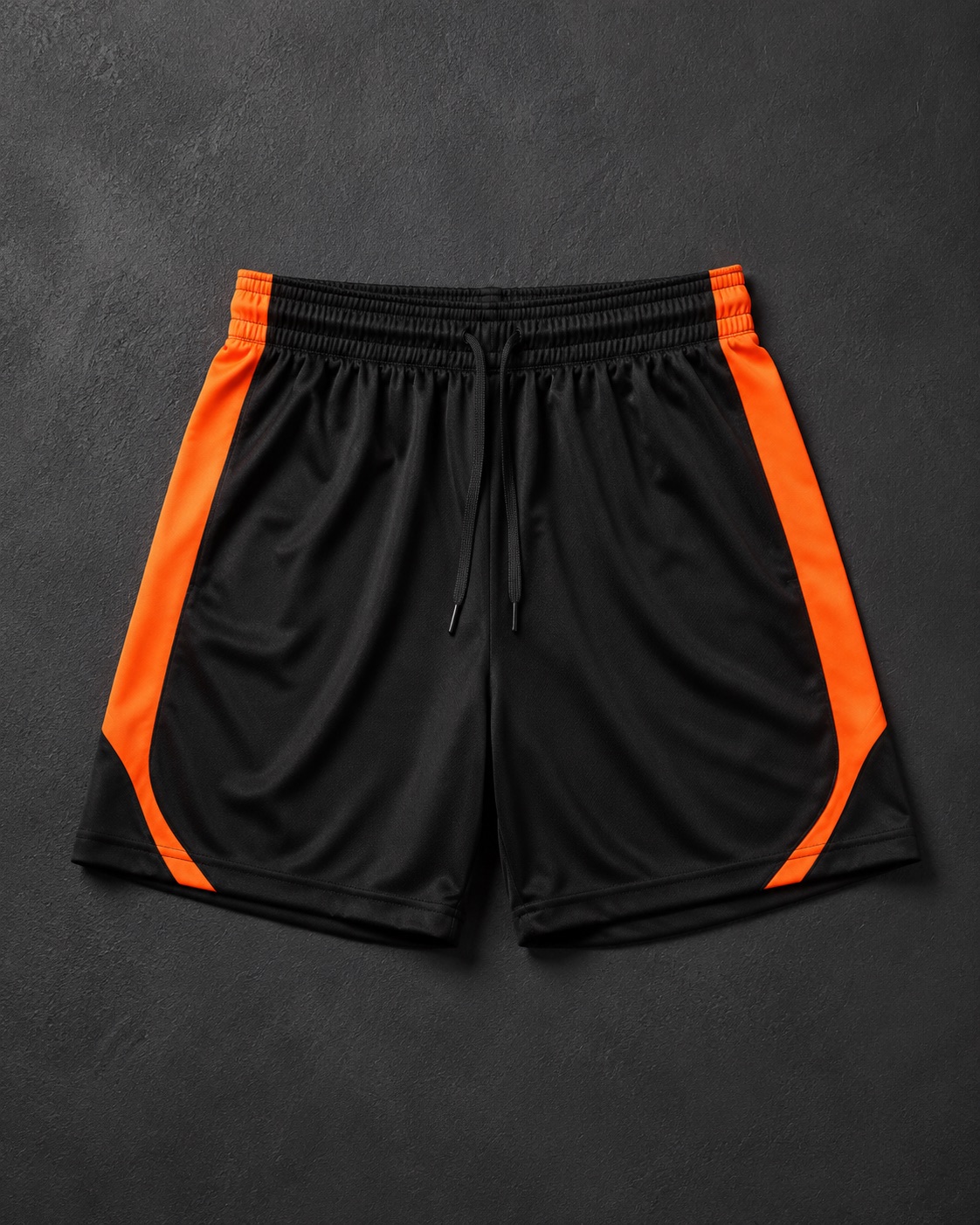Black football match shorts with orange trim, flat lay on dark charcoal