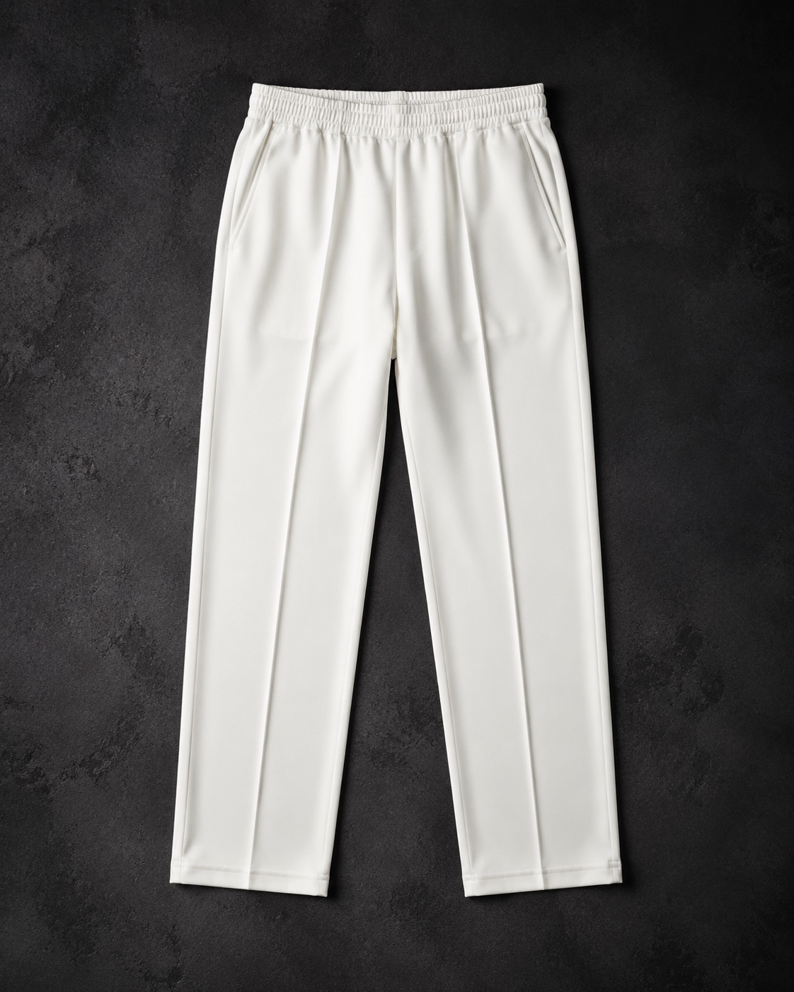 White cricket trousers with a pressed crease, flat lay on dark charcoal
