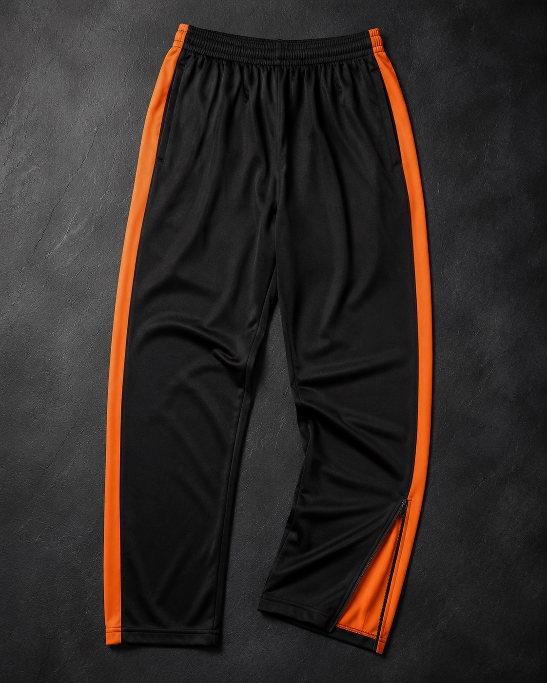 Athletics warm-up pants with a side zip, flat lay on dark charcoal