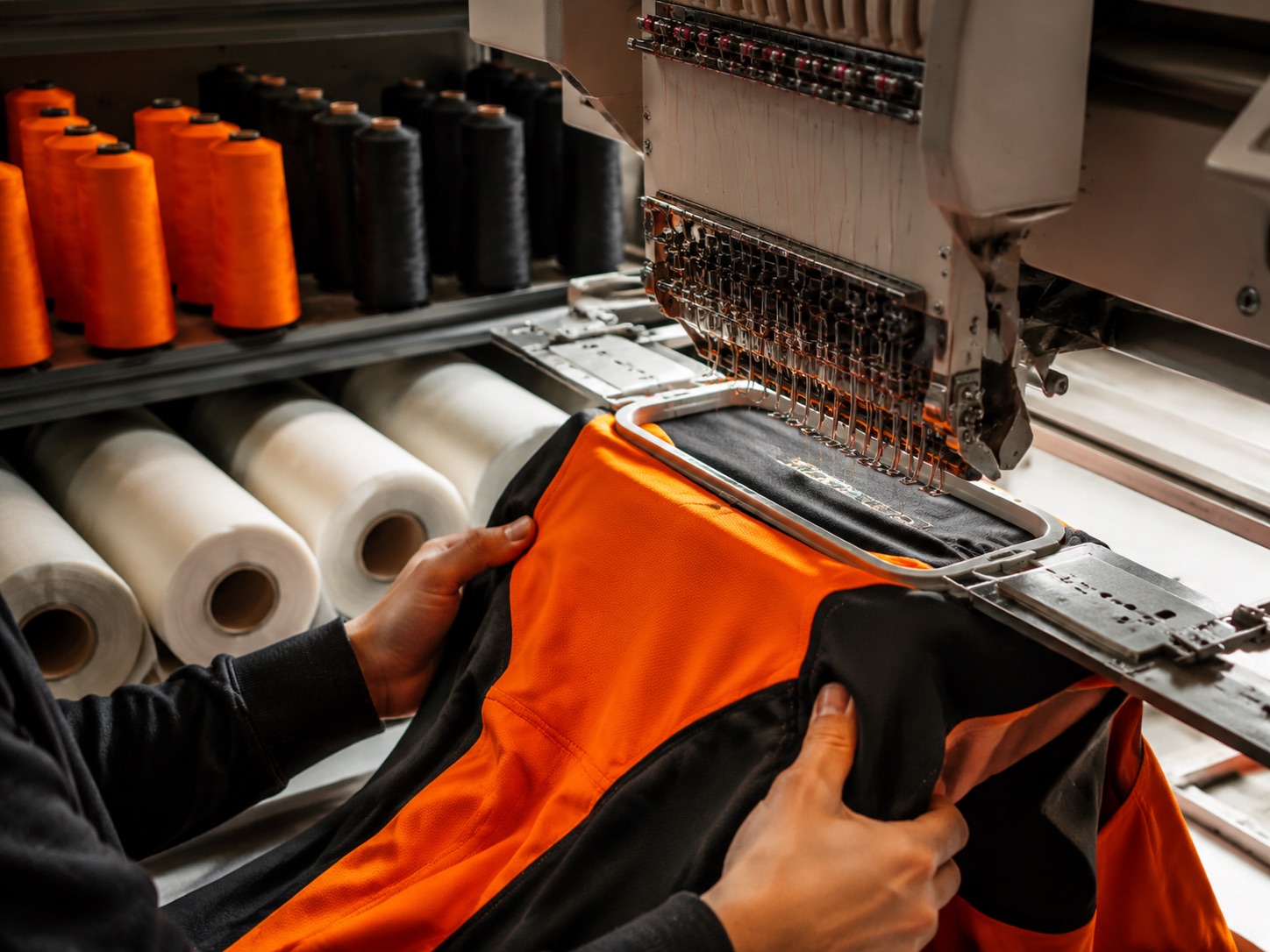 Rack of embroidery thread cones beside rolls of backing stabiliser