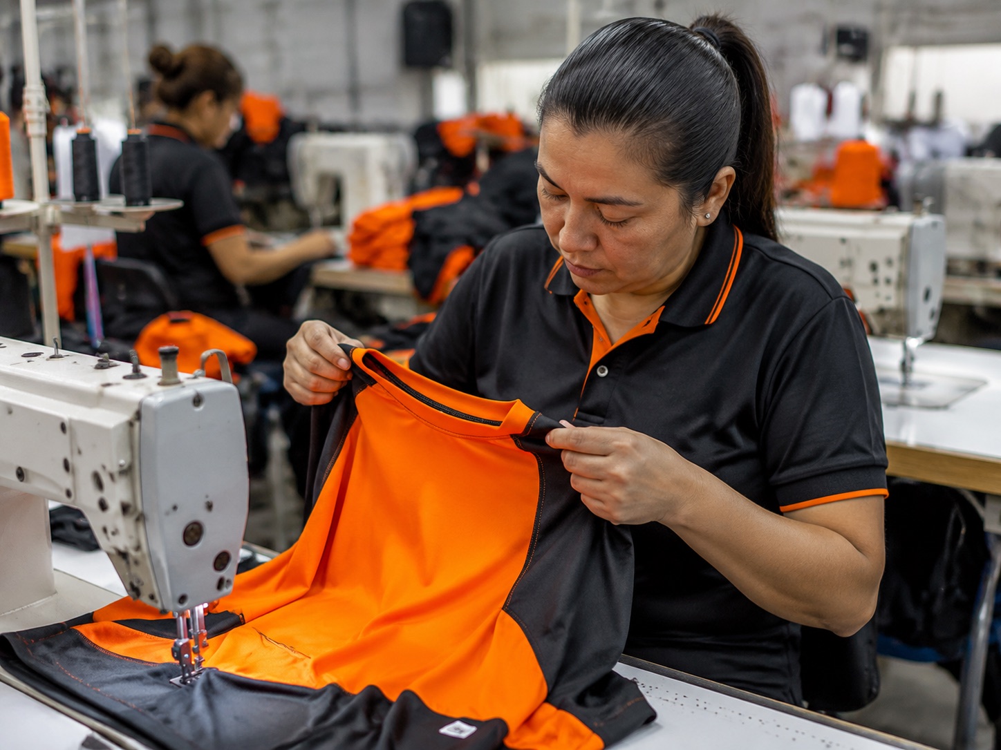 Line supervisor inspecting a partly assembled garment at a sewing station
