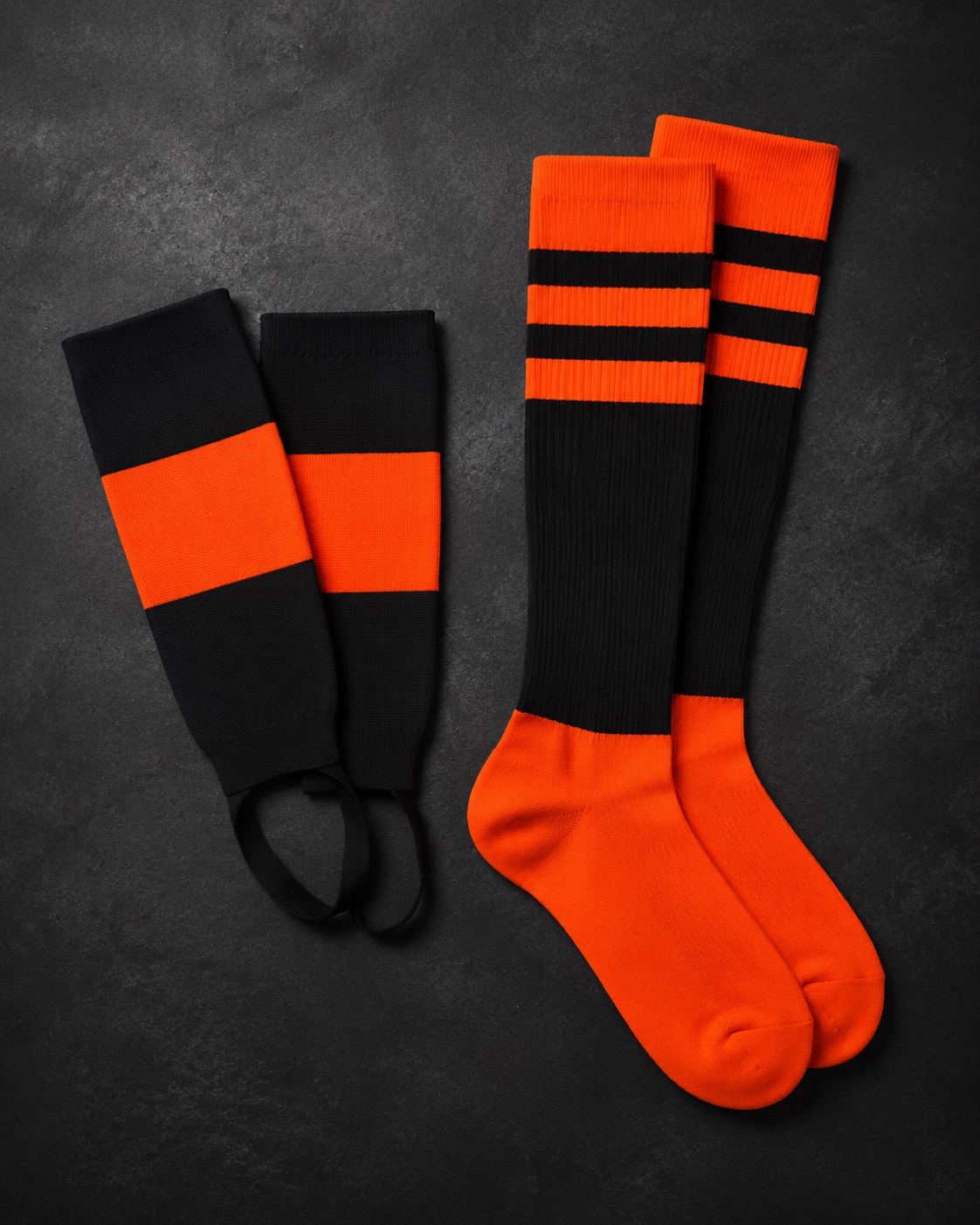 Baseball stirrups beside knitted team socks, flat lay on dark charcoal