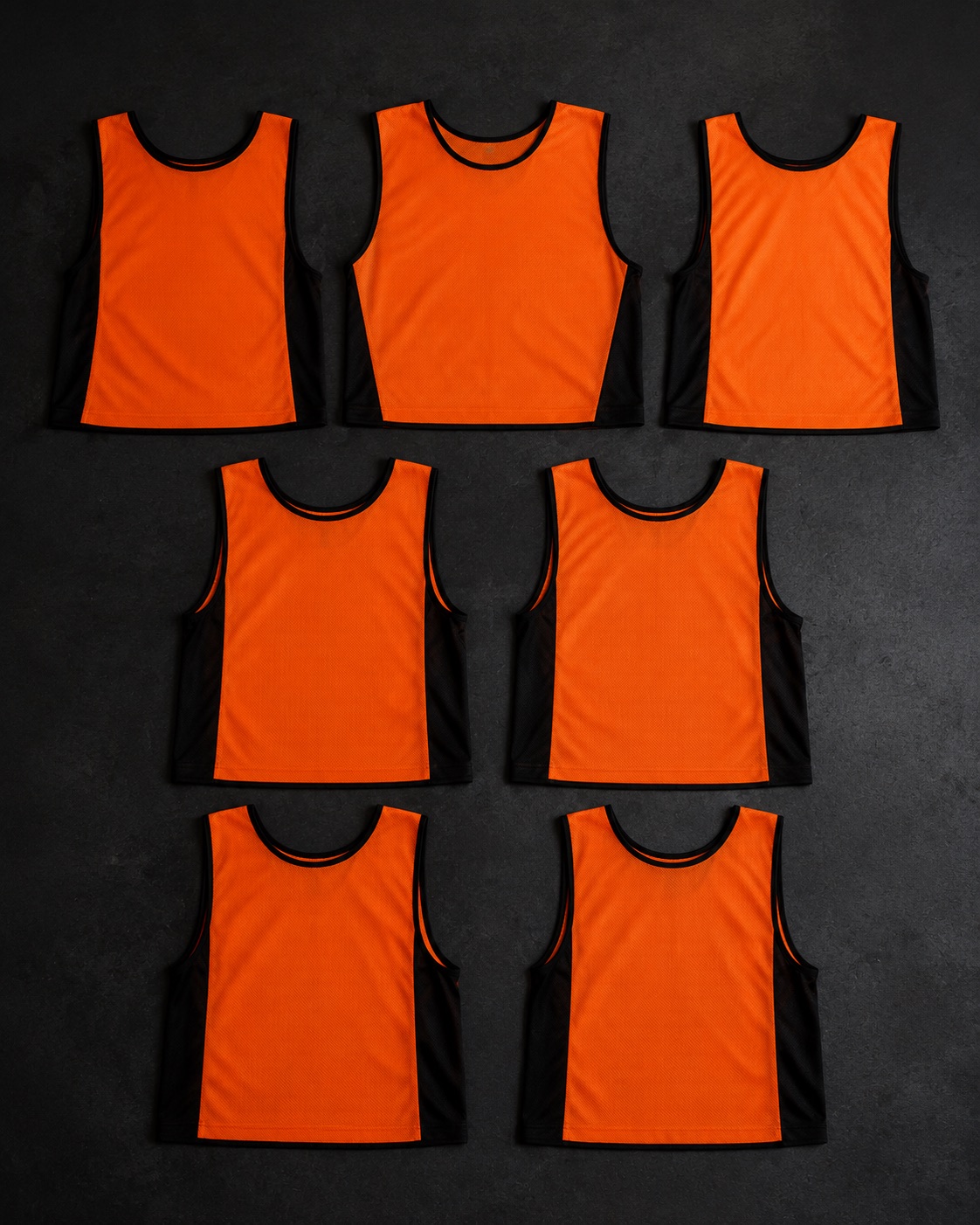 Set of seven netball position bibs laid out, flat lay on dark charcoal